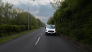 White Van Driving on Rural Road Under Cloudy Sky