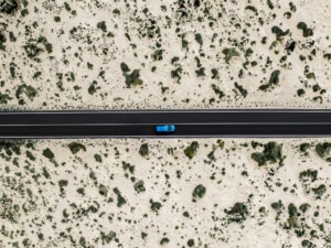 Blue coloured car driving through sand dunes on a highway shot from a drone point of view, Lanzarote, Canary Islands, Spain