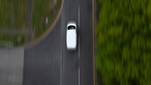 A white van drives along a country road, captured from above with a sense of motion, surrounded by lush greenery in an outdoor setting.