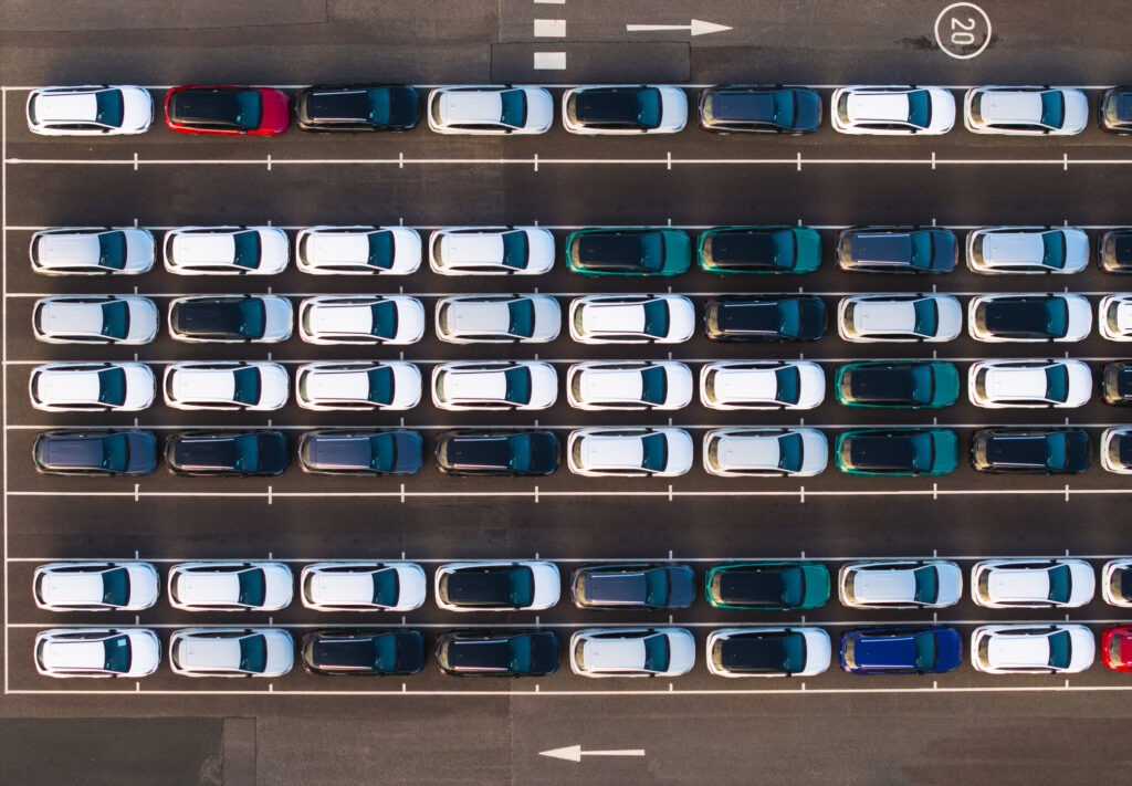 An aerial view directly above rows of newly built cars in the automobile industry on a commercial dock ready to be loaded for export and import with VAT and tariffs