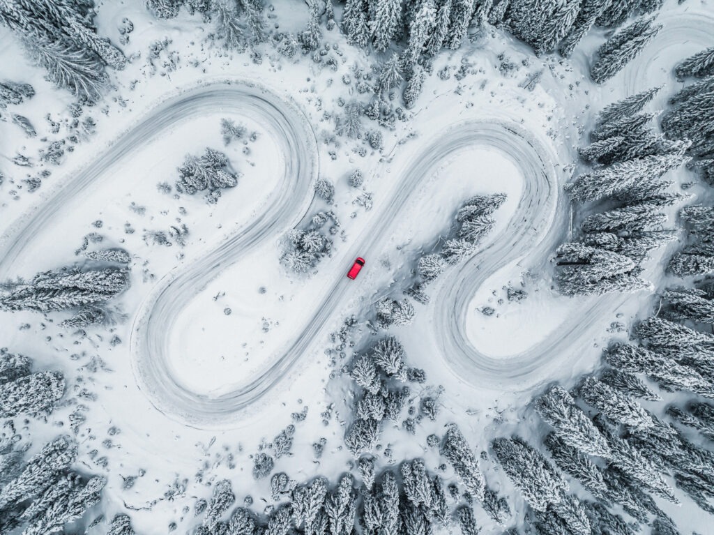 Car driving on a winding road through a snow covered forest seen from directly above, Dolomites, Italy