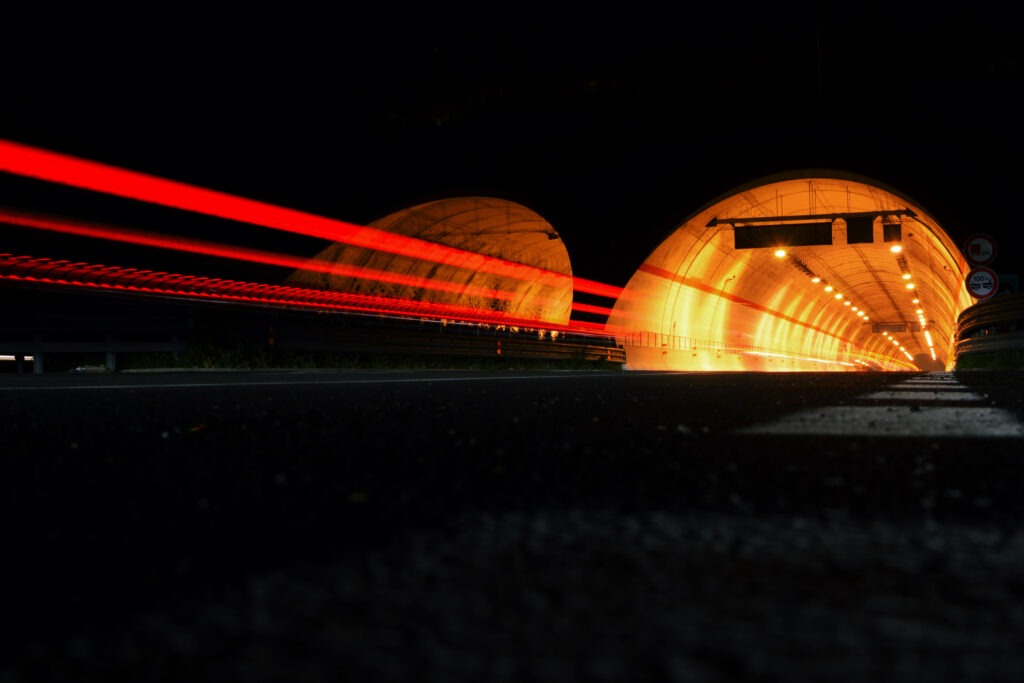 Street at night with red trails of cars in front of a tunnel