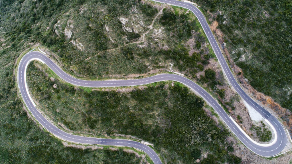 Empty long mountain road to the horizon on a sunny summer day at bright sunset - aerial drone shot.