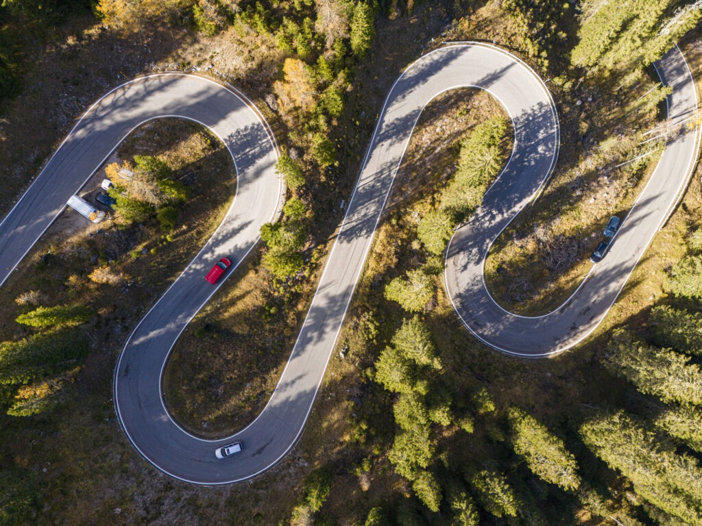 Luftaufnahme einer Straße, die sich durch einen dichten grünen Wald im Dolomiten-Nationalpark schlängelt, Drohnen-Panoramafoto des wunderschönen Gebirgspasses, versteckt im herbstlichen Kiefernwald mit dem sanften Licht des Herbstsonnenuntergangs, Dolomiten-Alpen, Südtirol, Italien