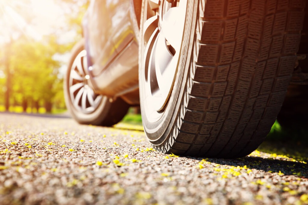 Car tires closeup on asphalt road on summer day at park. Vehicle outdoors in nature with beautiful sunlight.