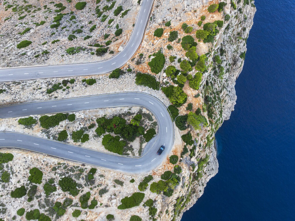 Drohnenbild eines Autos auf der Harpin-Kurve über der Klippe am Meer, Halbinsel Cap de Formentor, Sierra de Tramuntana, Pollenca, Mallorca, Balearen, Mittelmeer, Spanien