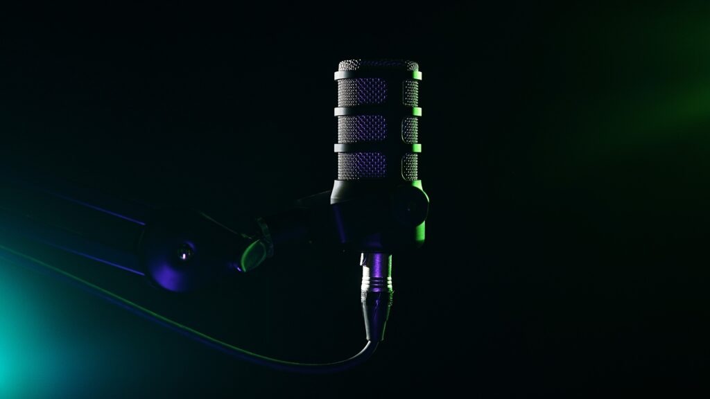 Ein dynamisches Studiomikrofon an einem Galgenarm, beleuchtet durch stimmungsvolles grünes und violettes Licht vor einem dunklen Hintergrund. Ideal für Podcasting, Sprachaufzeichnung und Rundfunk.