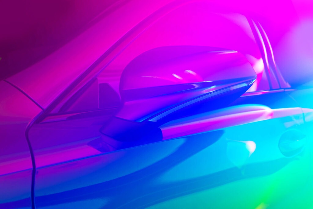 A close-up of a modern car side mirror and bodywork illuminated by vibrant blue and pink neon light.