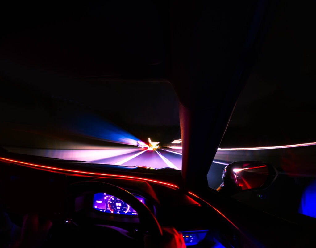 Point of view from inside a moving car driving through a highway at night with long exposure light trails.