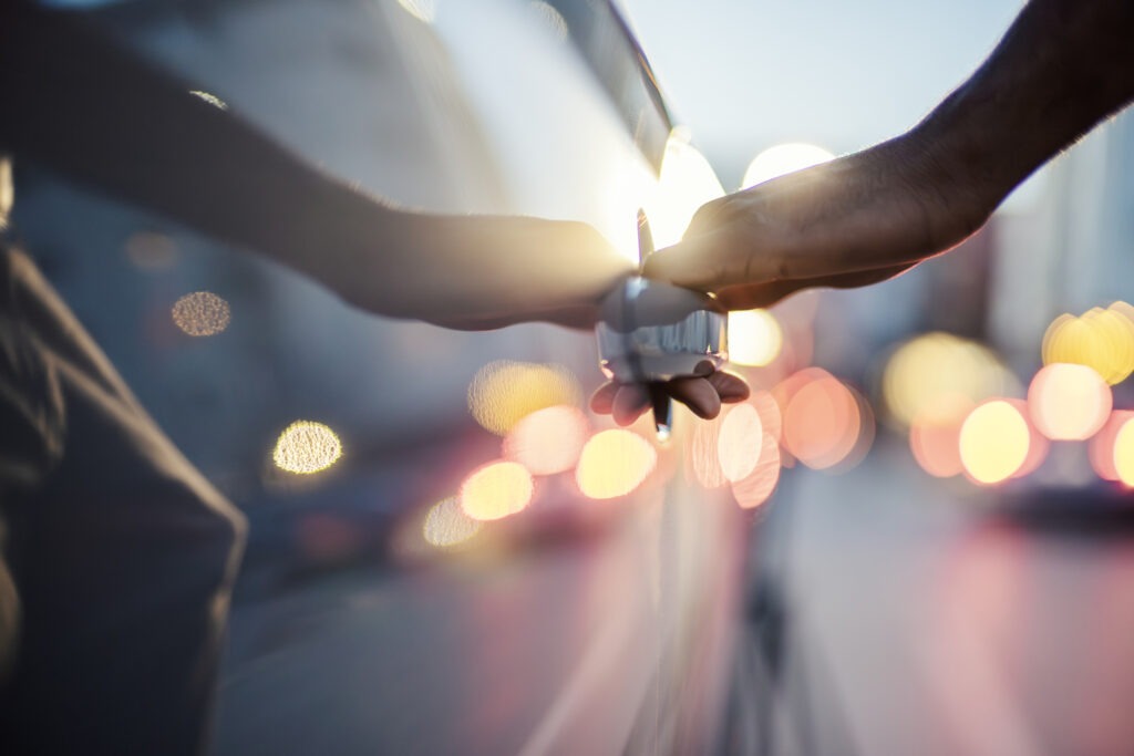 Human hand opening a car door with abstract city lights creating a colorful bokeh background, symbolizing urban travel, late evening commutes, lifestyle, and arrival at a destination