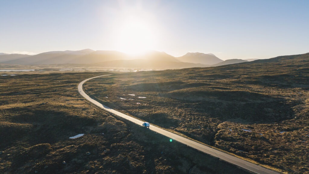 An aerial/drone view of a van on the road (A82) through Glencoe in the Scottish Highlands at sunrise on a bright winter's morning