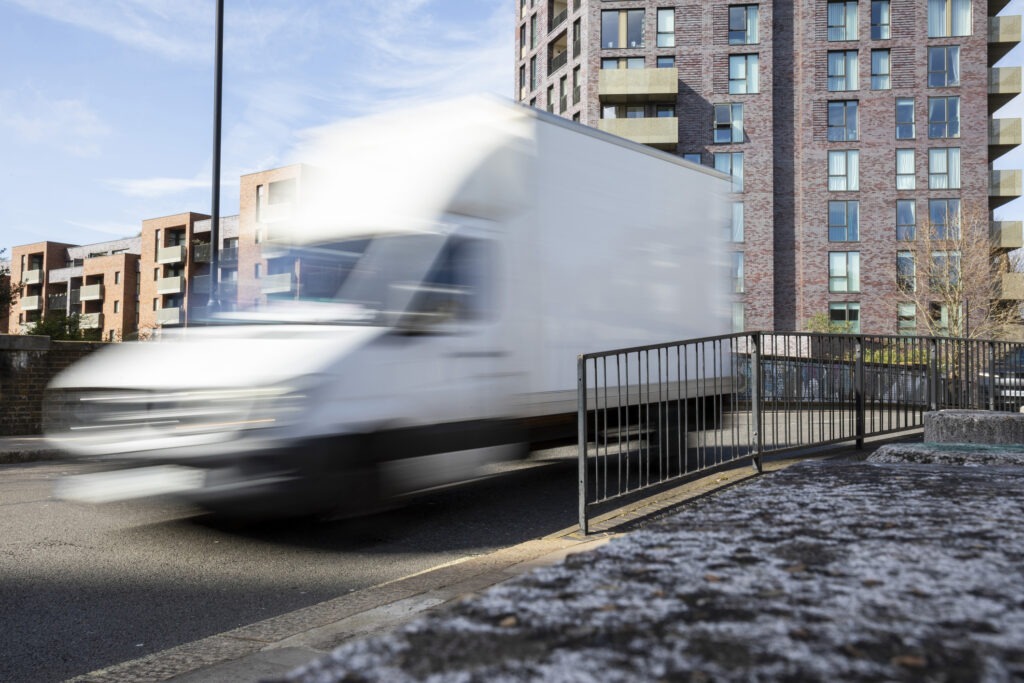 White delivery van with blurred motion on an urban road by a tower block