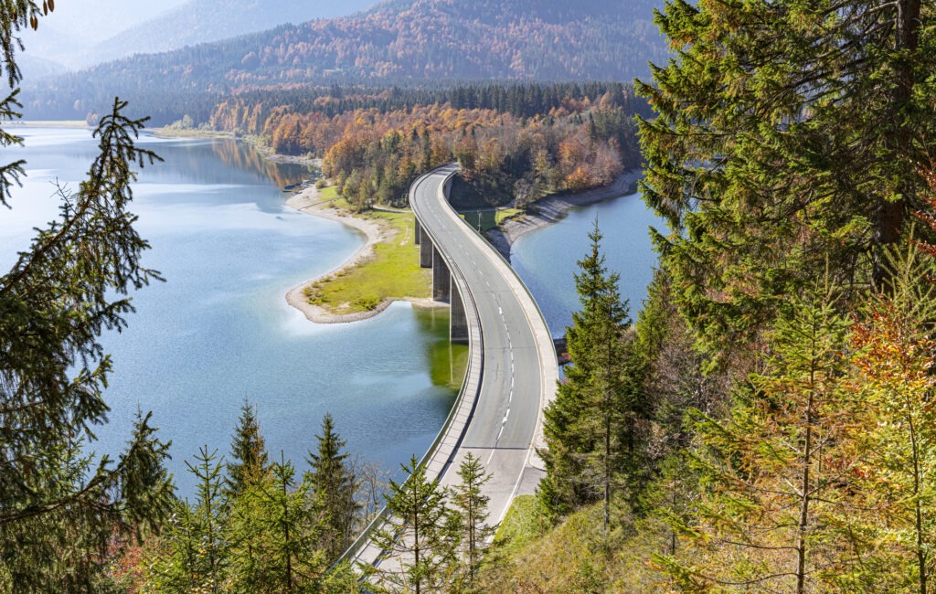 Epic curved bridge in Bavaria seen from above in front of a lake and mountain range while autumn - horizontal wide shot.