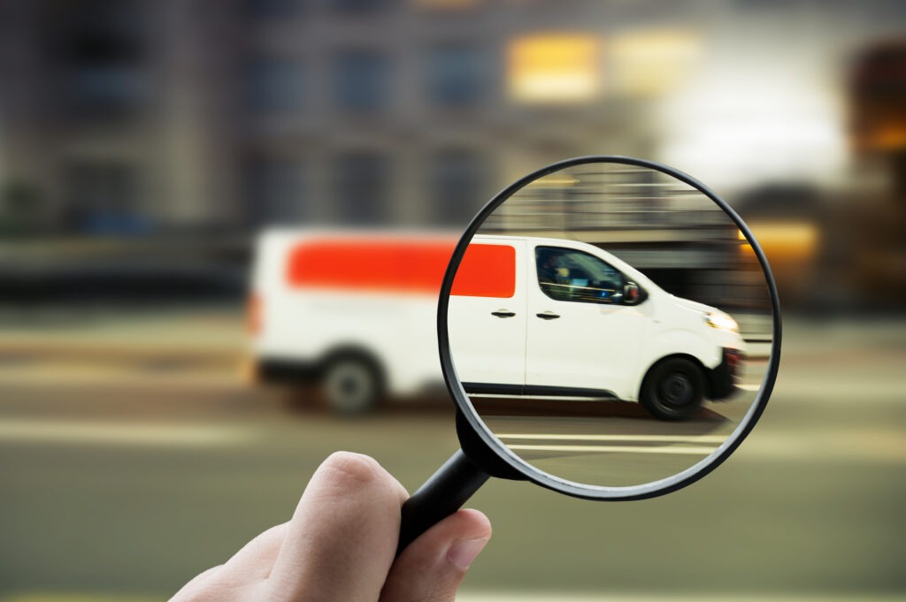 Eine Lupe mit Fokus auf einen weißen Lieferwagen, der durch die Stadt fährt und Logistik und städtischen Verkehr repräsentiert.
